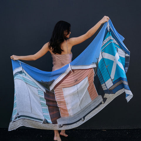 girl holding out a  Brighton Beach scarf stretched out in from of a dark black wall.