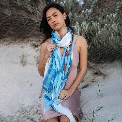 Girl sitting down in the coastal dunes wearing a cotton linen scarf with a design of Cicerello's in Fremantle Harbour