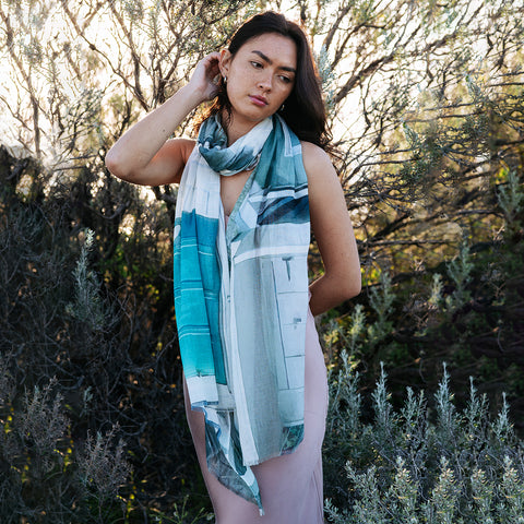A girl standing in the bushes wearing a cotton linen scarf featuring Portsea Beach boatsheds in greens and greys.